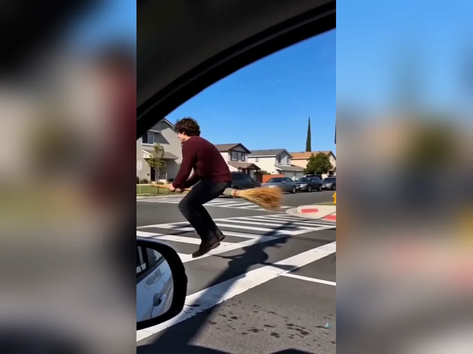 Broom rider in a burgundy sweater hovering over the road alongside the car window